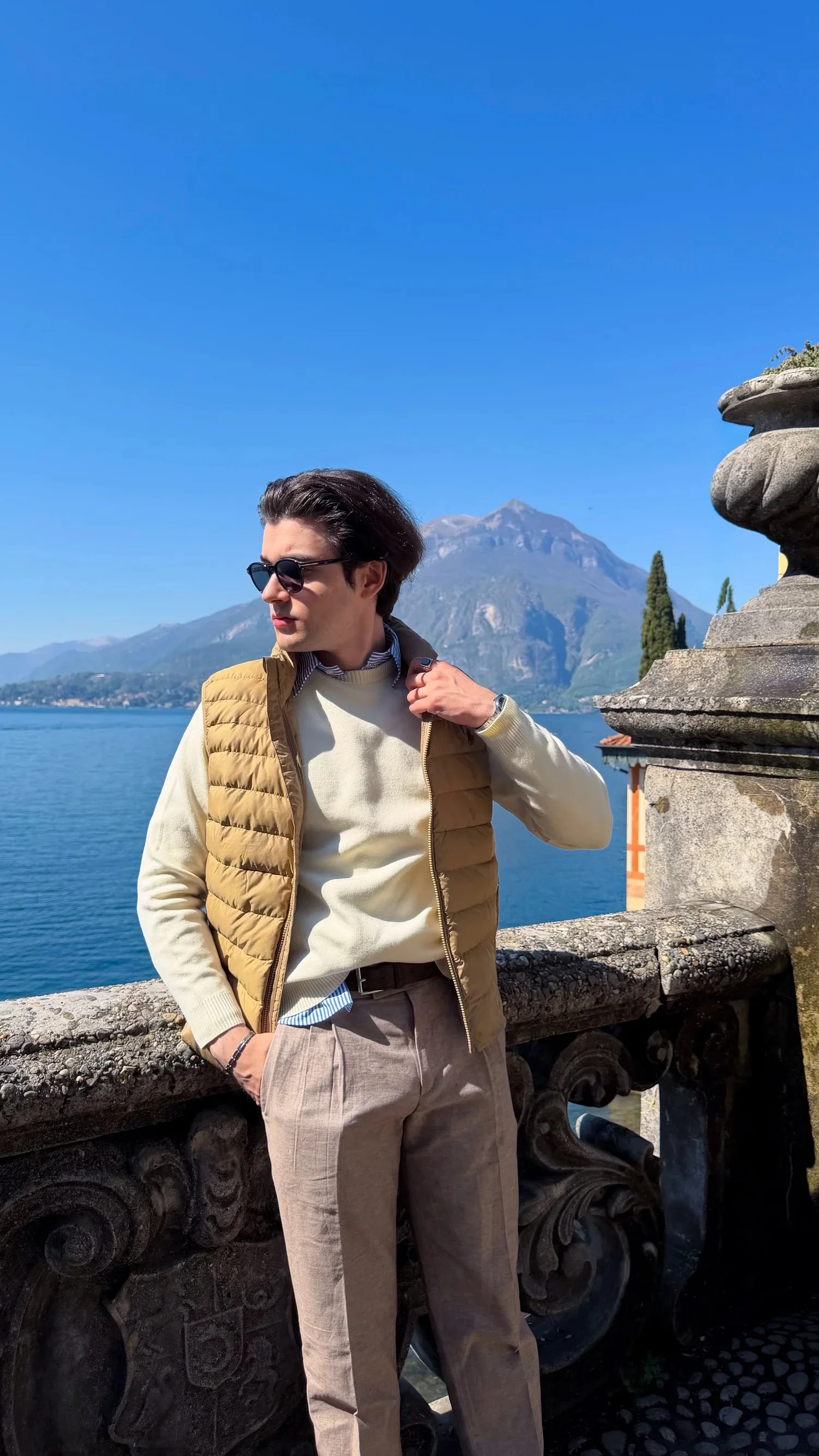 A person wearing sunglasses beside a stone balustrade overlooking a lake.