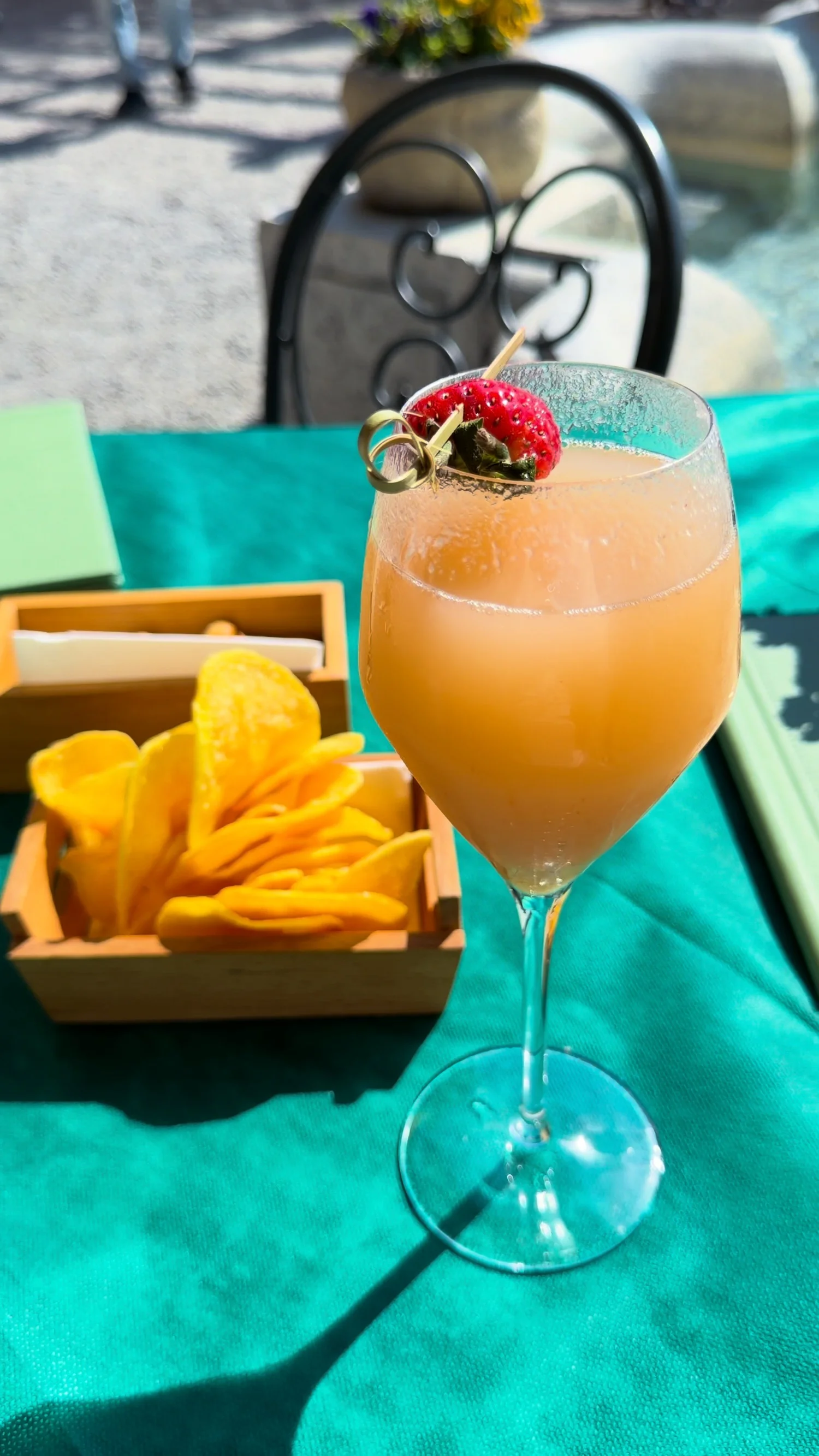 An orange cocktail garnished with fruit beside a bowl of crisps.