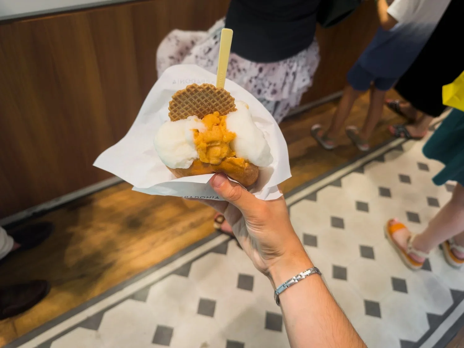 Gelato and a wafer held over a patterned floor inside a shop.