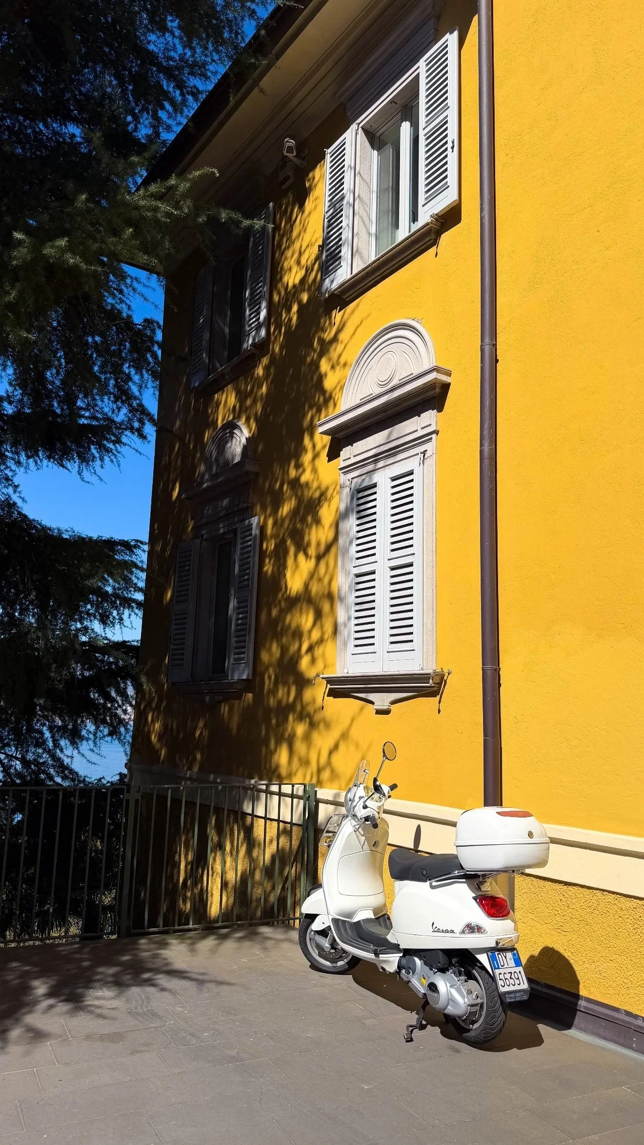 A white scooter parked beside a yellow villa wall.