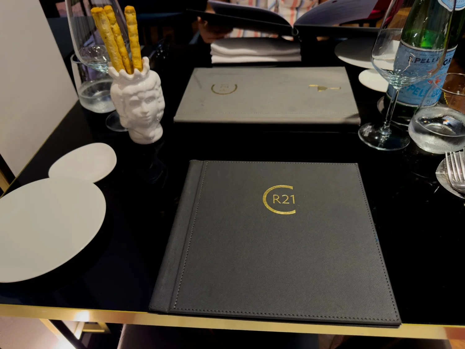 CR21 menus and a white ceramic head-shaped breadstick holder on a black table.