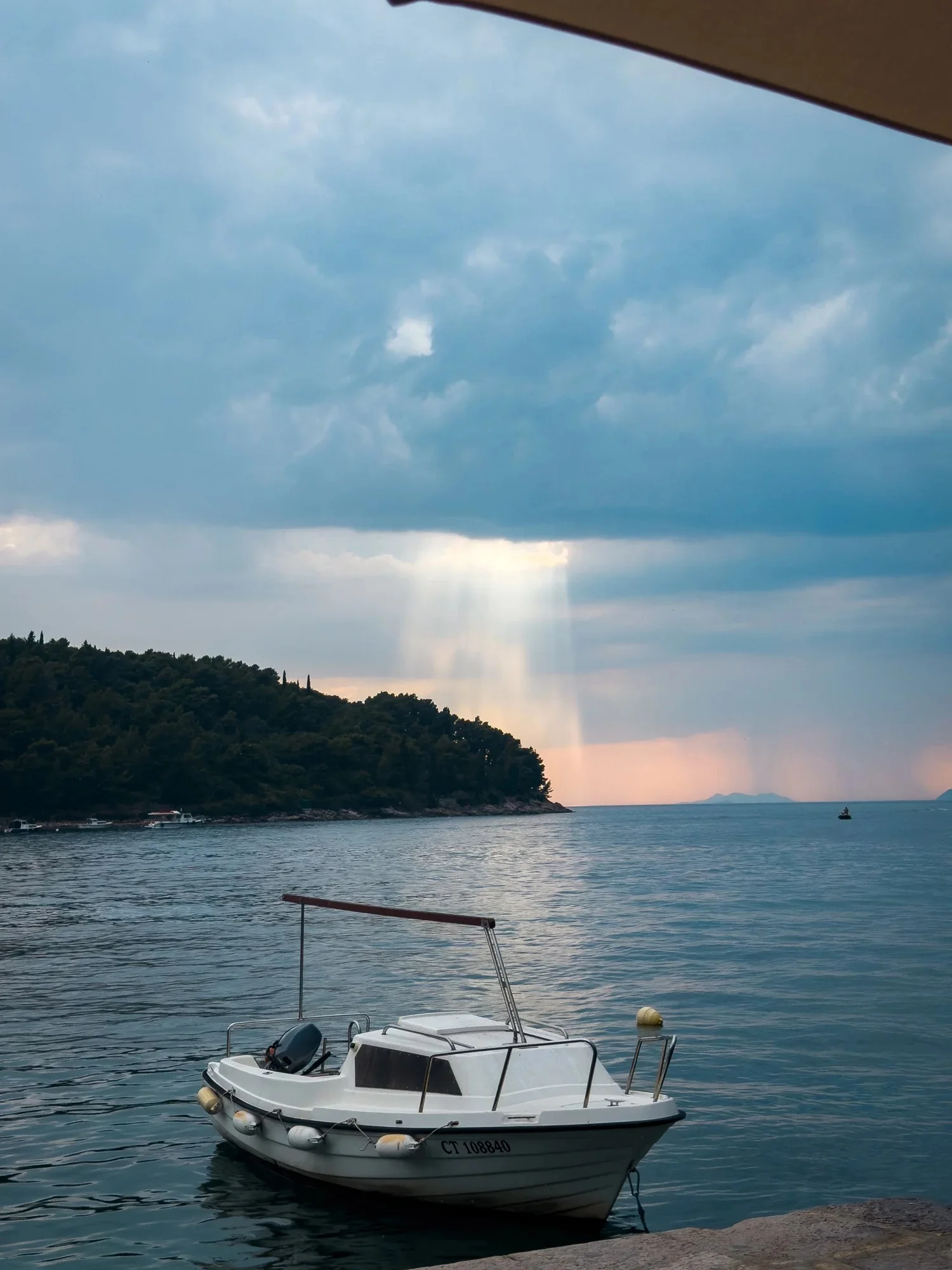 A small boat moored beside a waterfront beneath an evening sky.