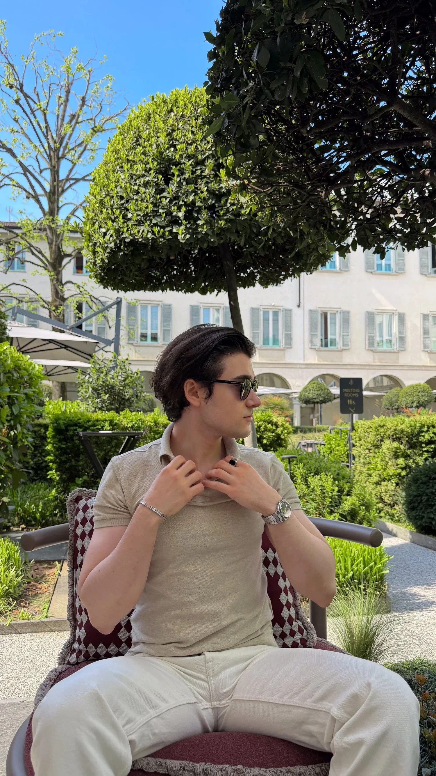 A person seated in a sunny courtyard surrounded by clipped trees.