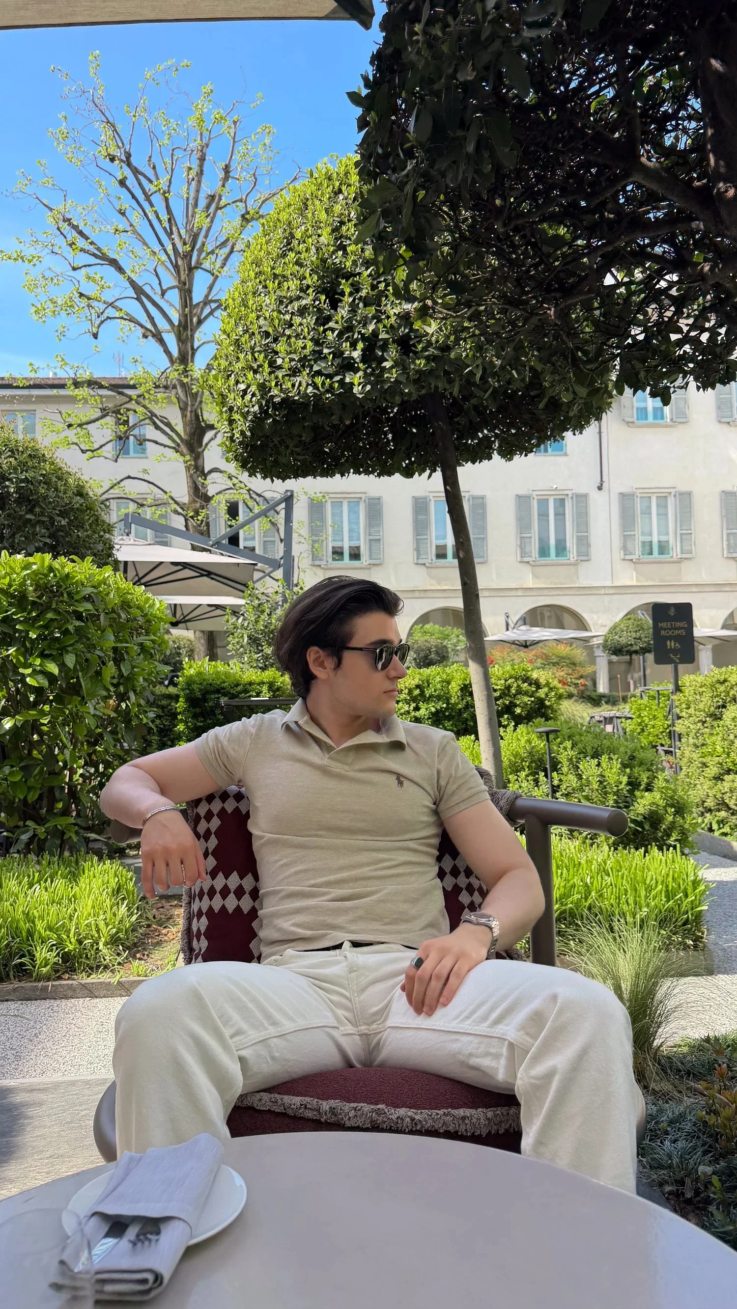 A person seated beneath a clipped tree in a hotel courtyard.