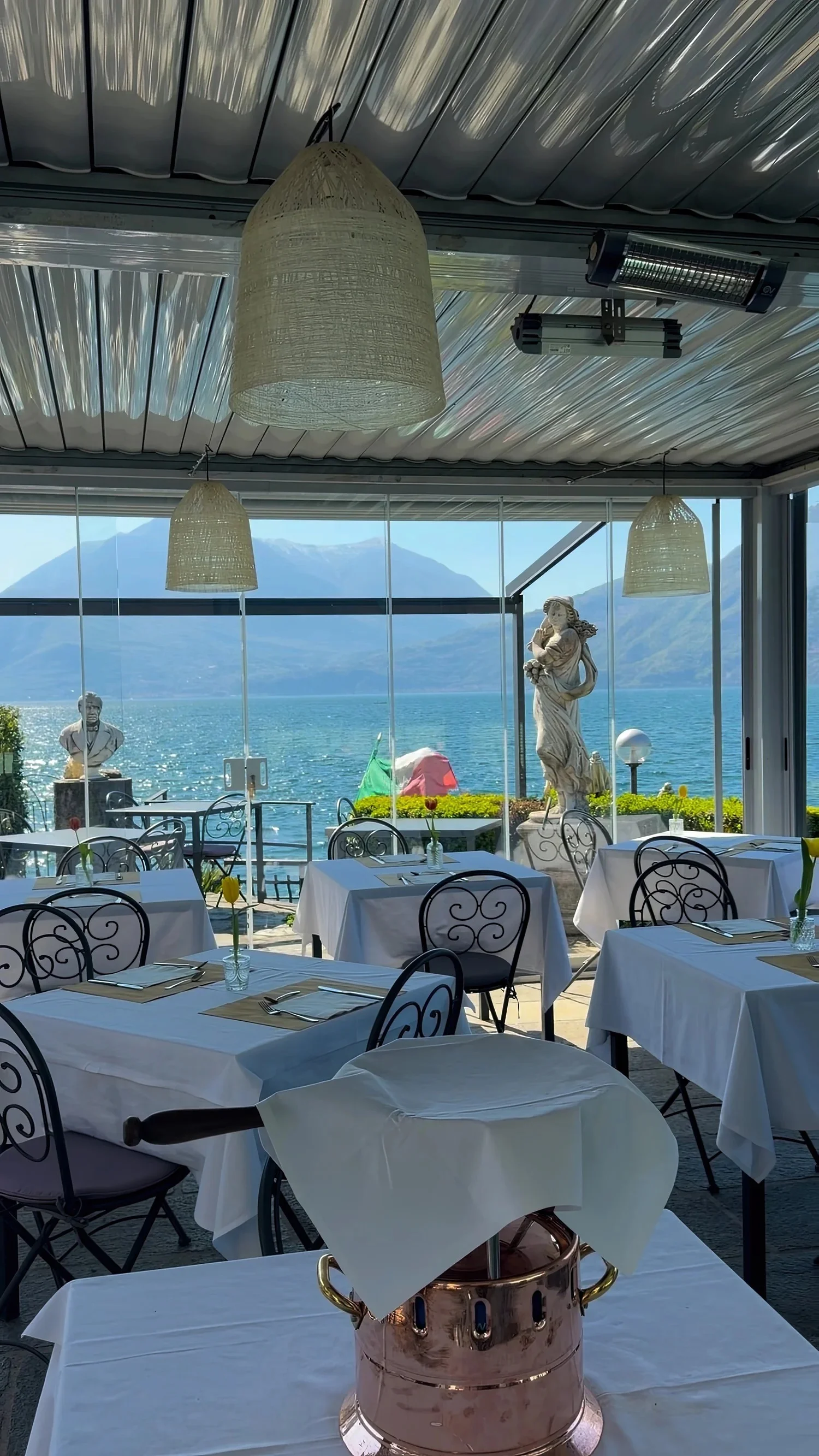 White-clothed dining tables beside large windows overlooking a lake.
