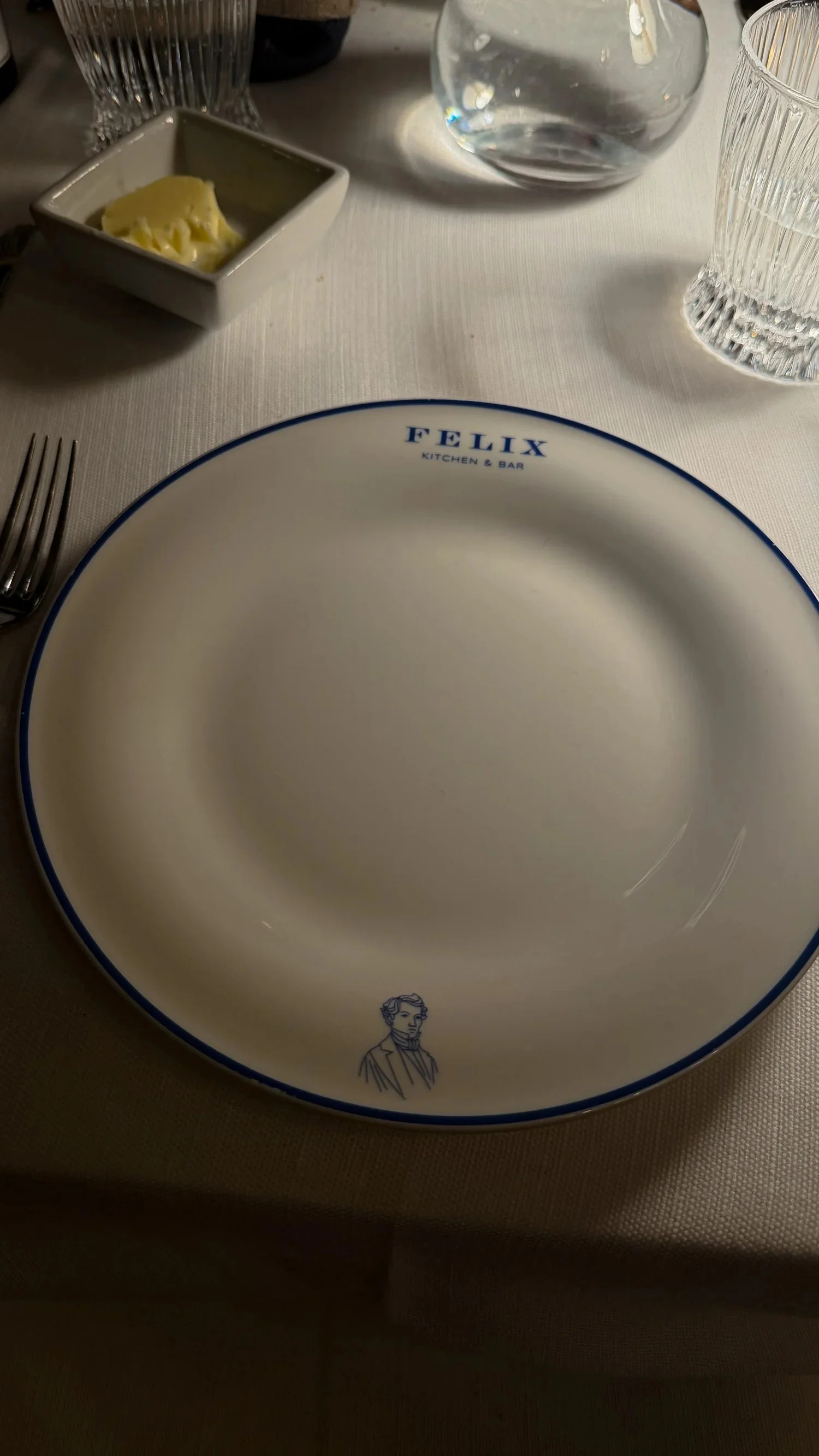 A white FELIX plate and silver cutlery set on a dining table.