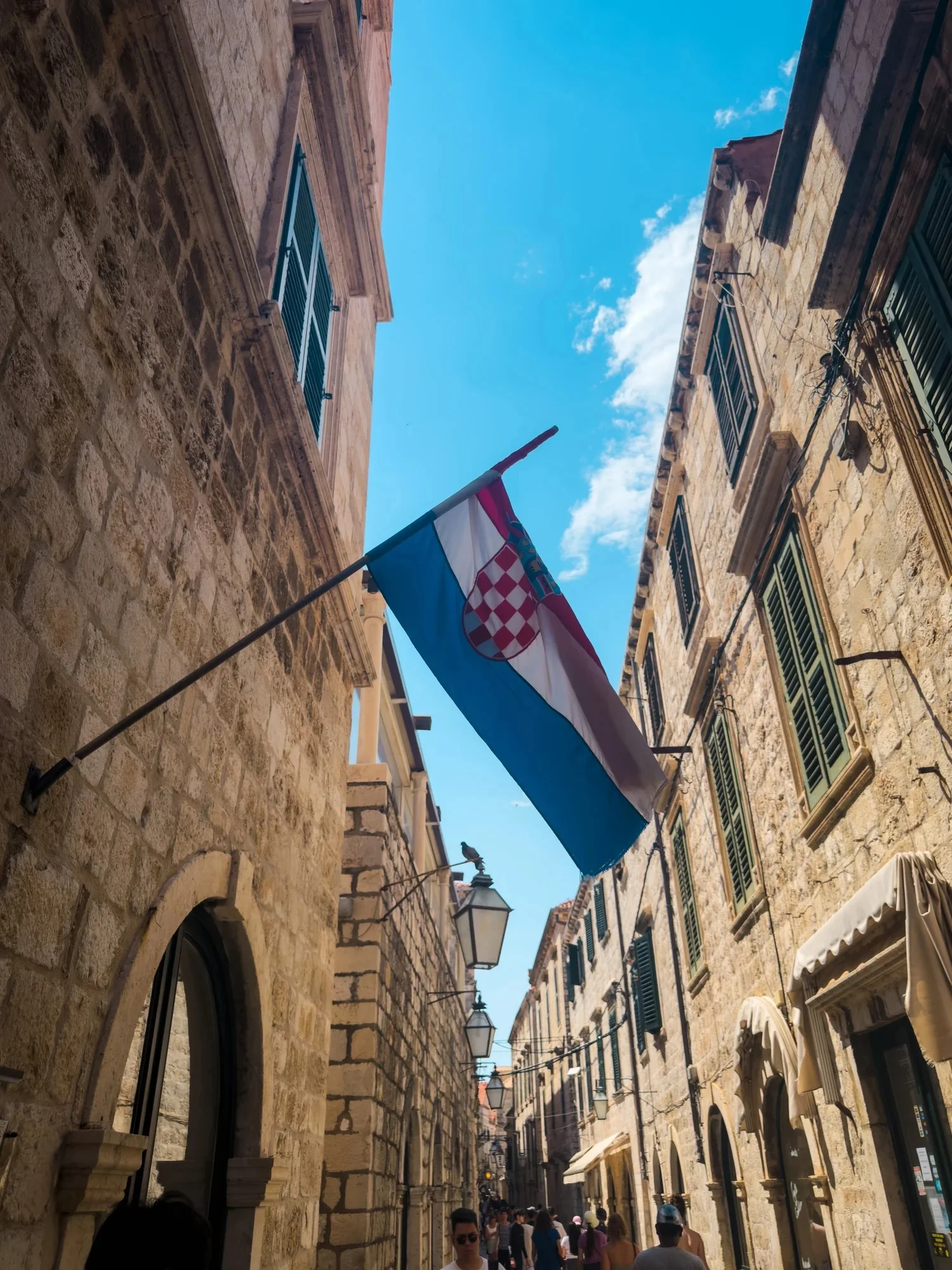 A narrow stone street with flags hanging between historic buildings.