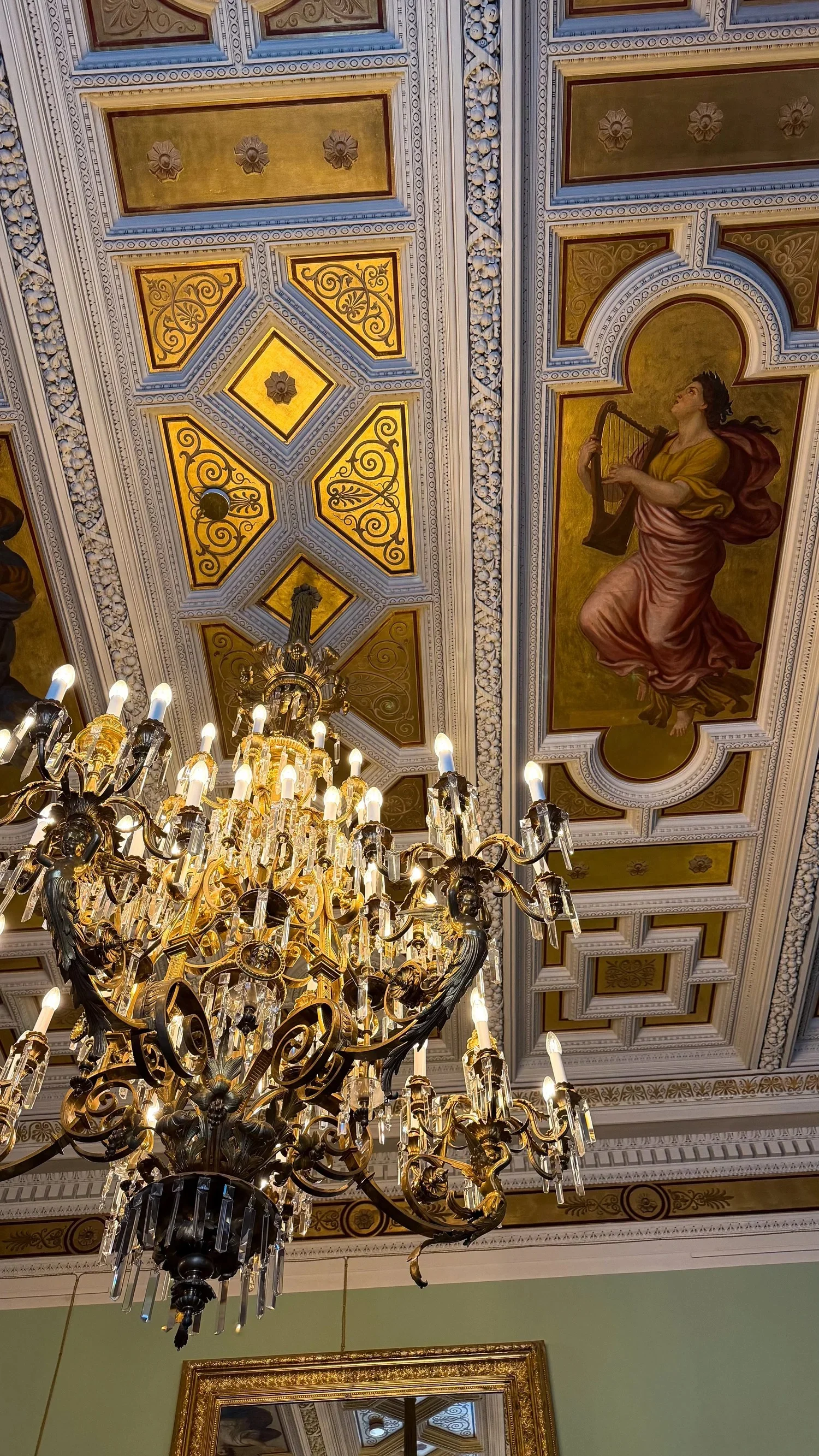 A chandelier hanging below decorative ceiling panels and painted figures.