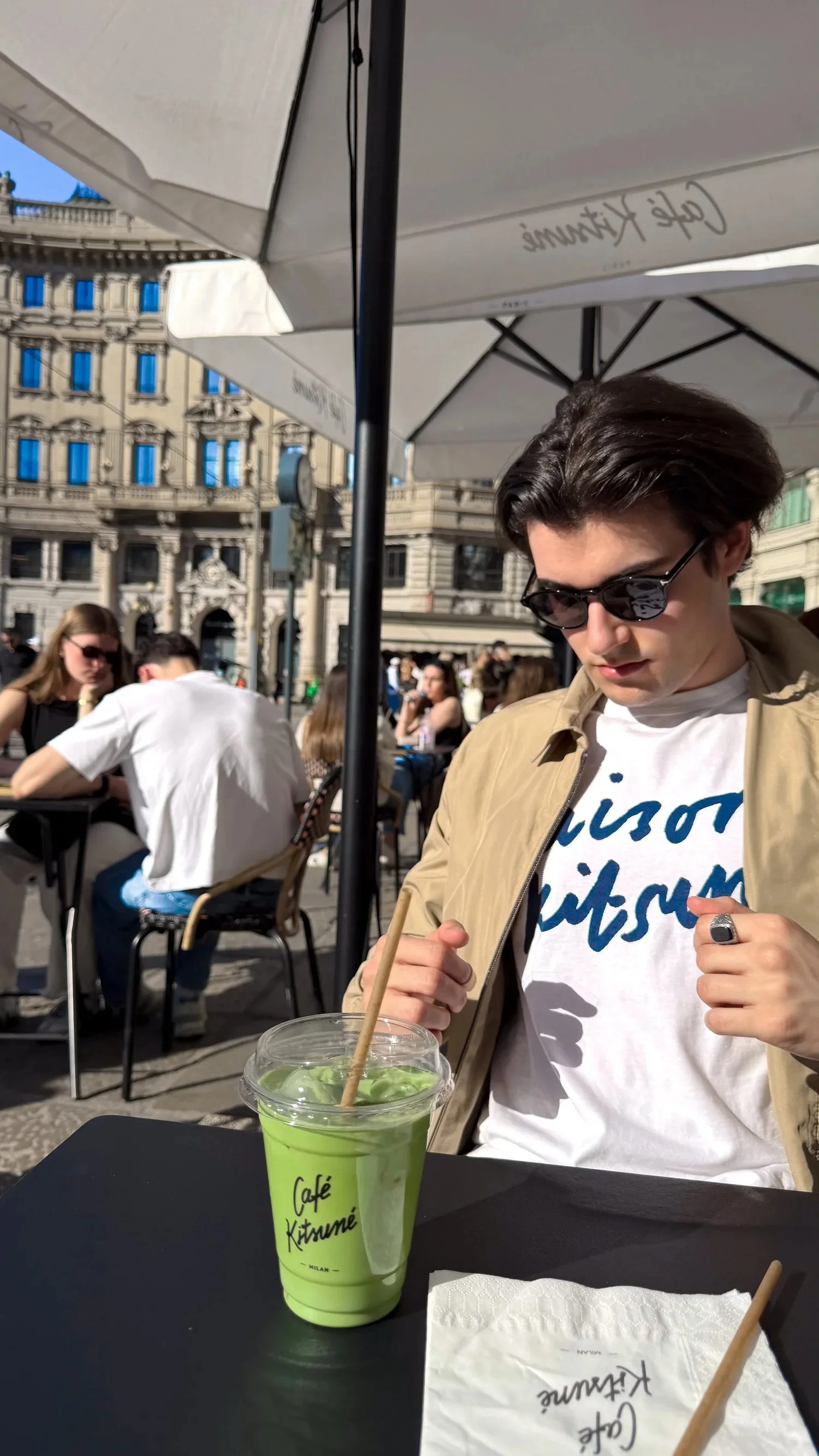 A person wearing sunglasses with a green drink at a café table.