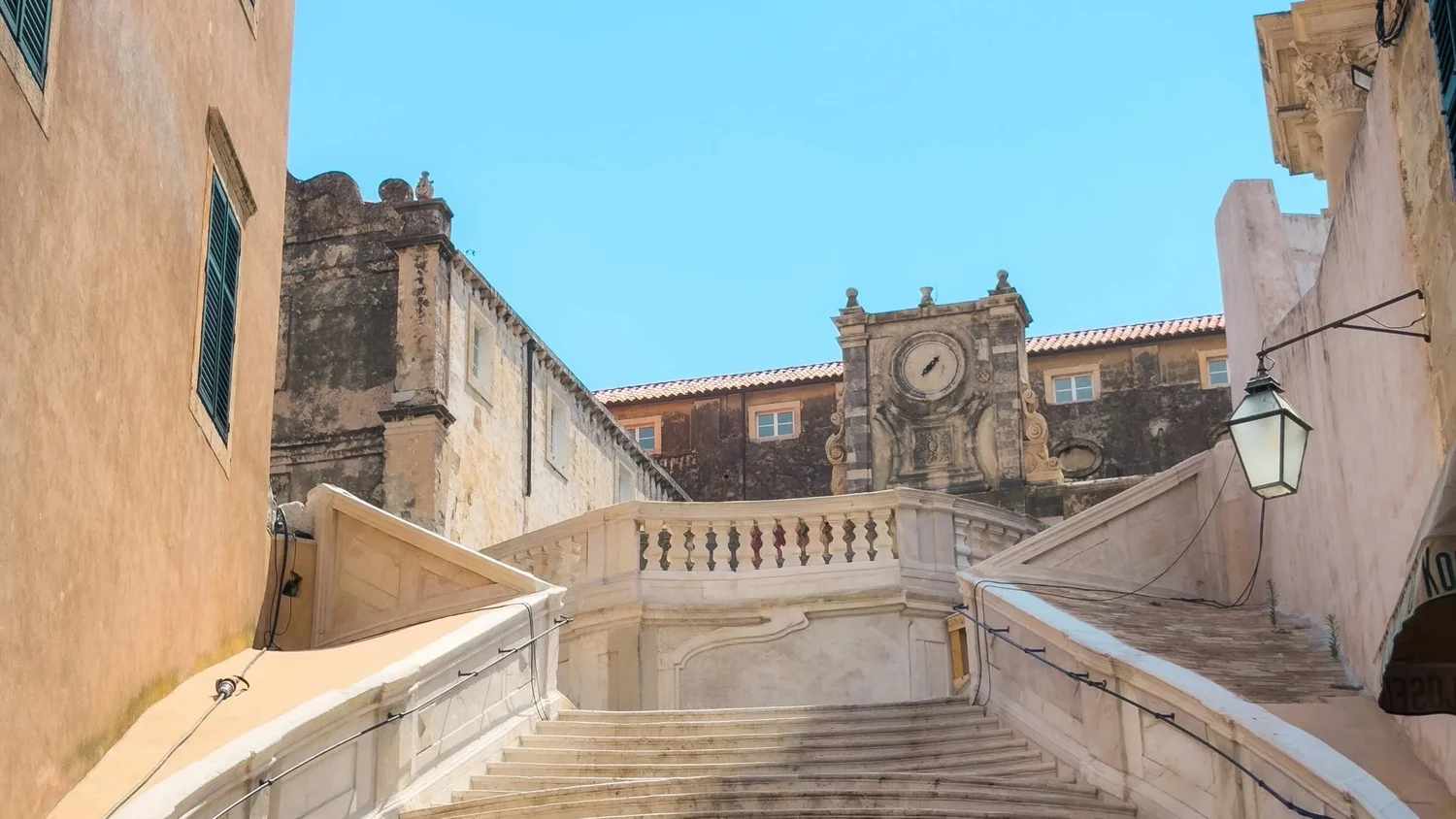 Stone staircase leading to a historic courtyard with a clock and balustrade.