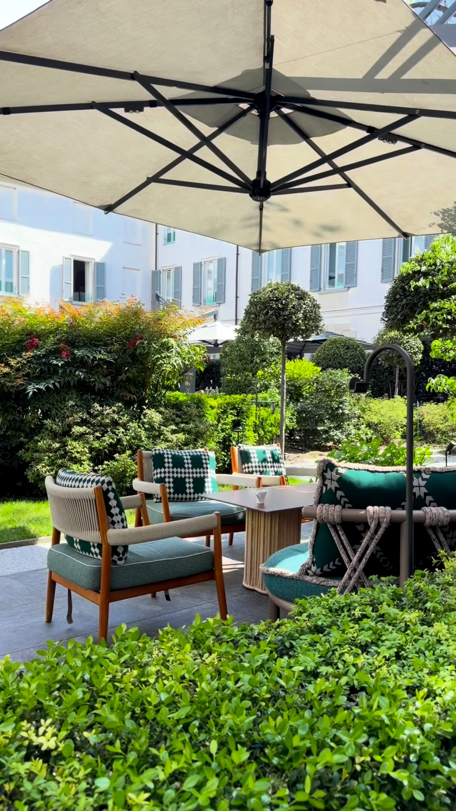 Outdoor tables beneath an umbrella in a green hotel courtyard.