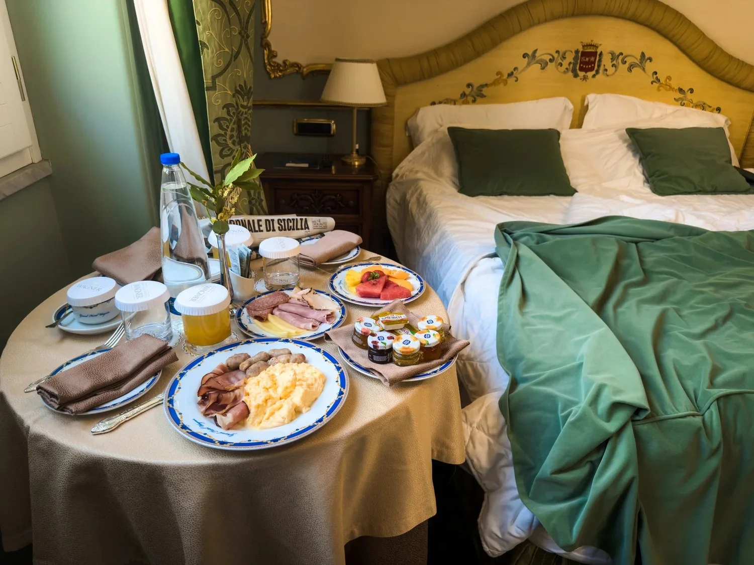Breakfast served on a table beside a green-covered hotel bed.