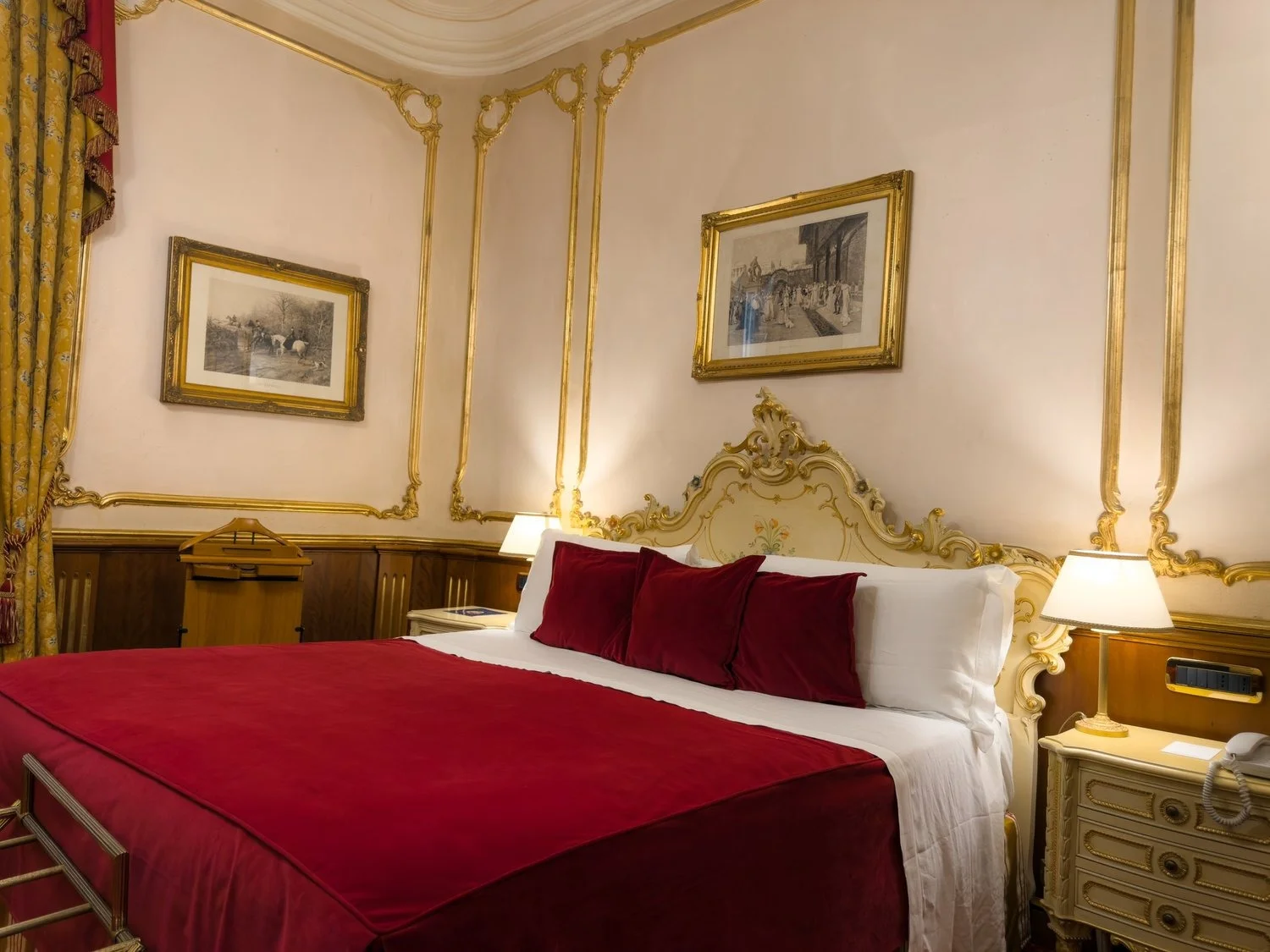 Hotel bedroom with a red bedspread and ornate cream-and-gold headboard.
