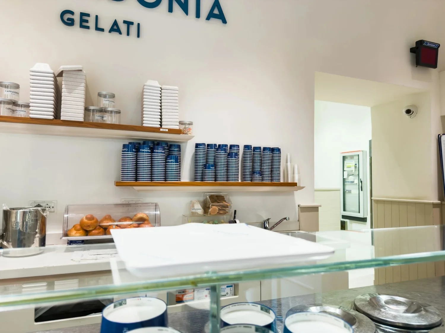 Gelato counter with stacked cups, water bottles and metal serving containers.