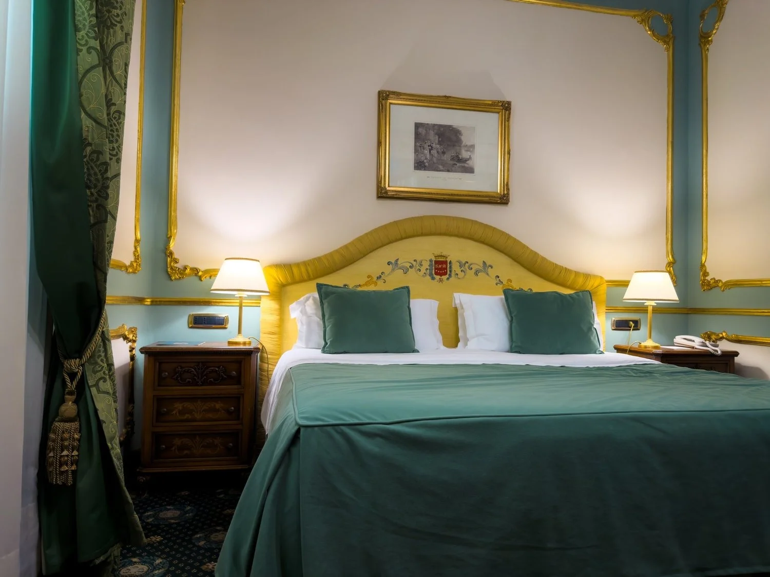 Hotel bedroom with a green bedspread and ornate yellow headboard.