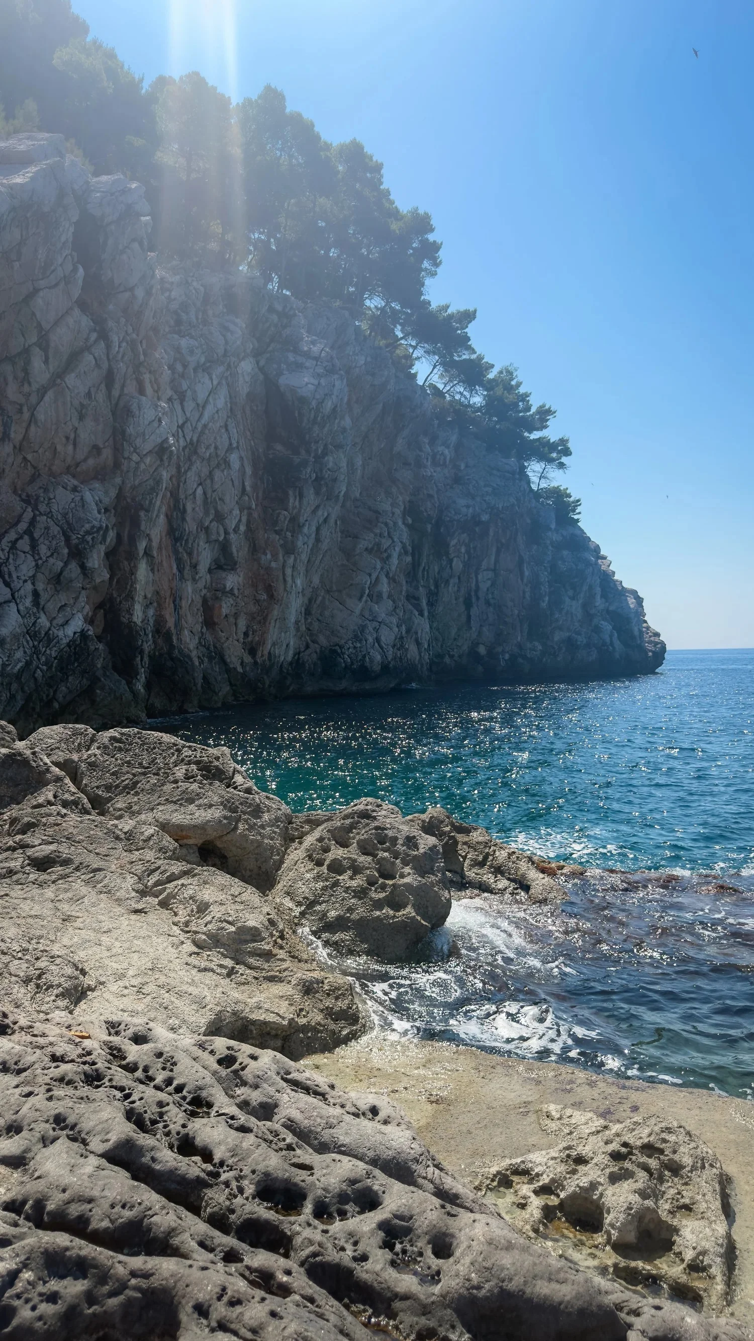 A rocky swimming spot beneath a steep seaside cliff.
