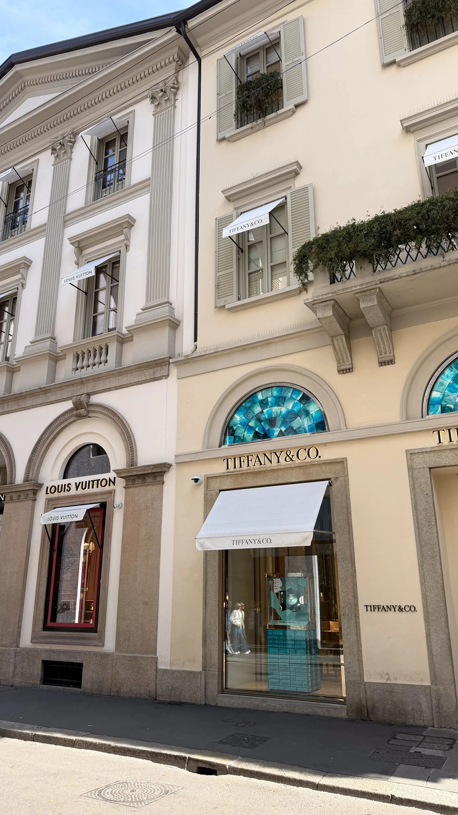 A pale shopfront with arched windows and a striped awning.