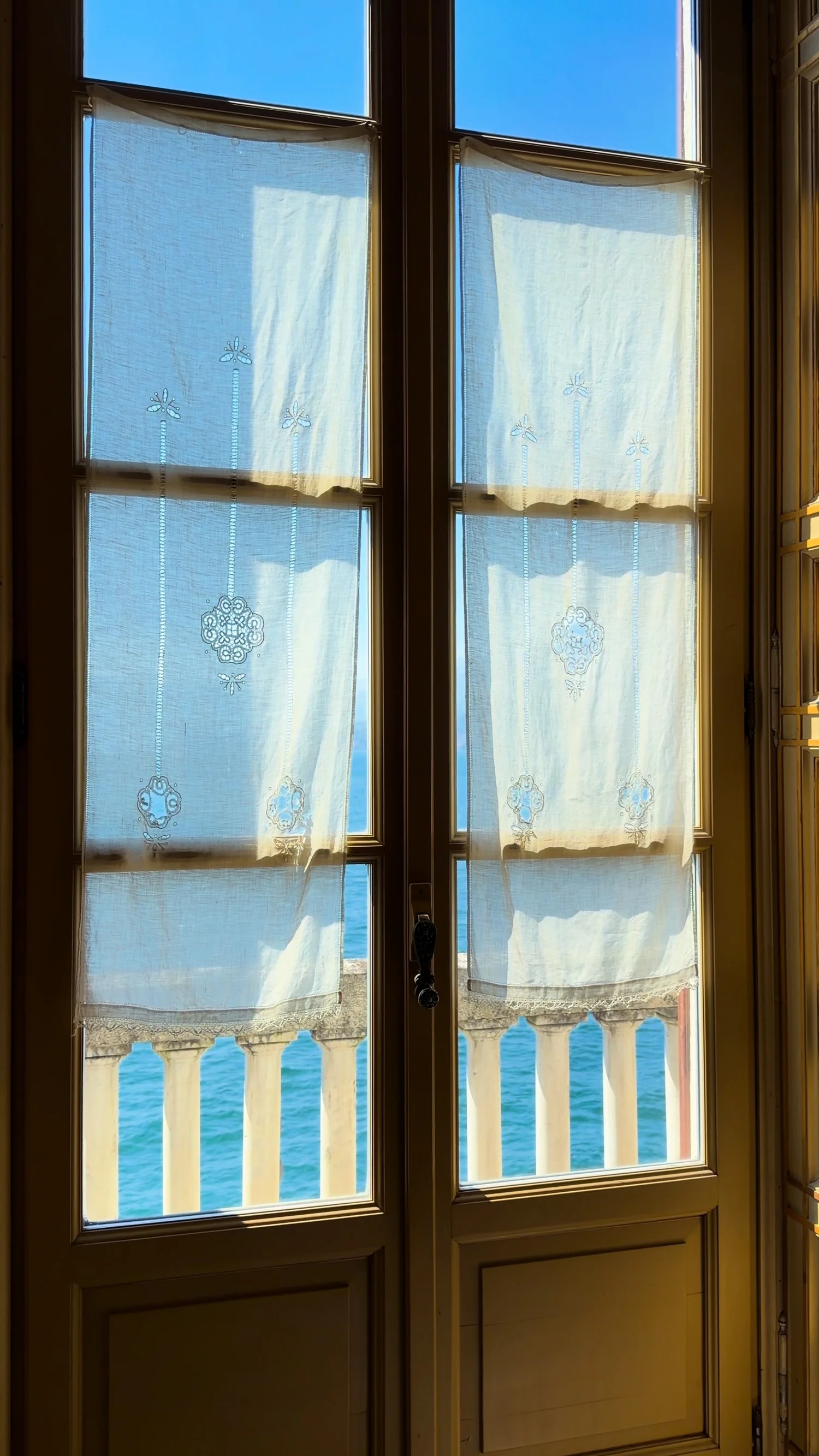 Lake light visible through tall wooden doors with sheer curtains.