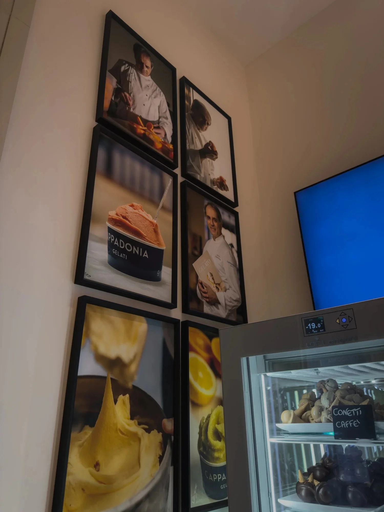 Framed photographs displayed beside a refrigerated cabinet in a gelato shop.