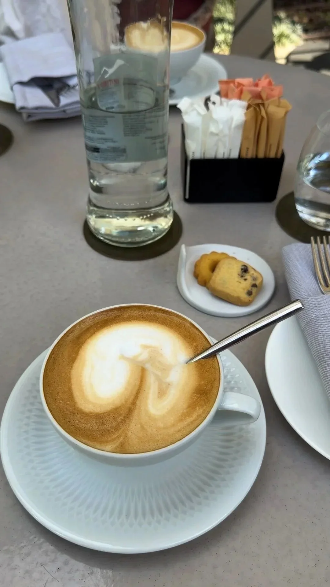 A cappuccino and small biscuit on an outdoor table.