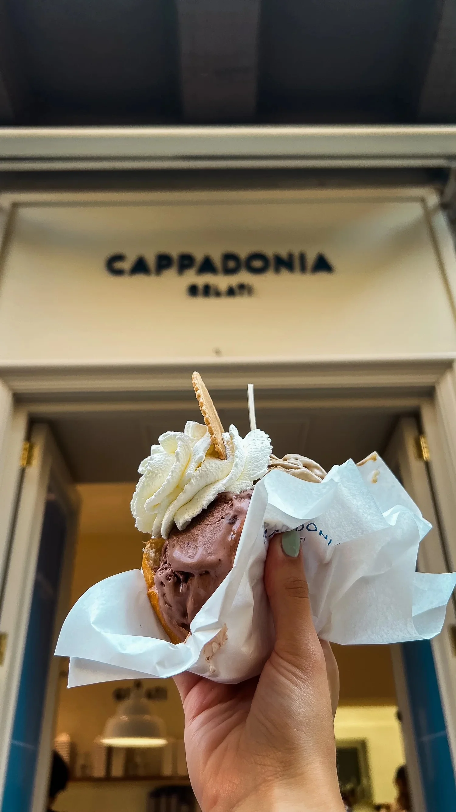 A hand holding gelato in brioche outside Cappadonia Gelati.