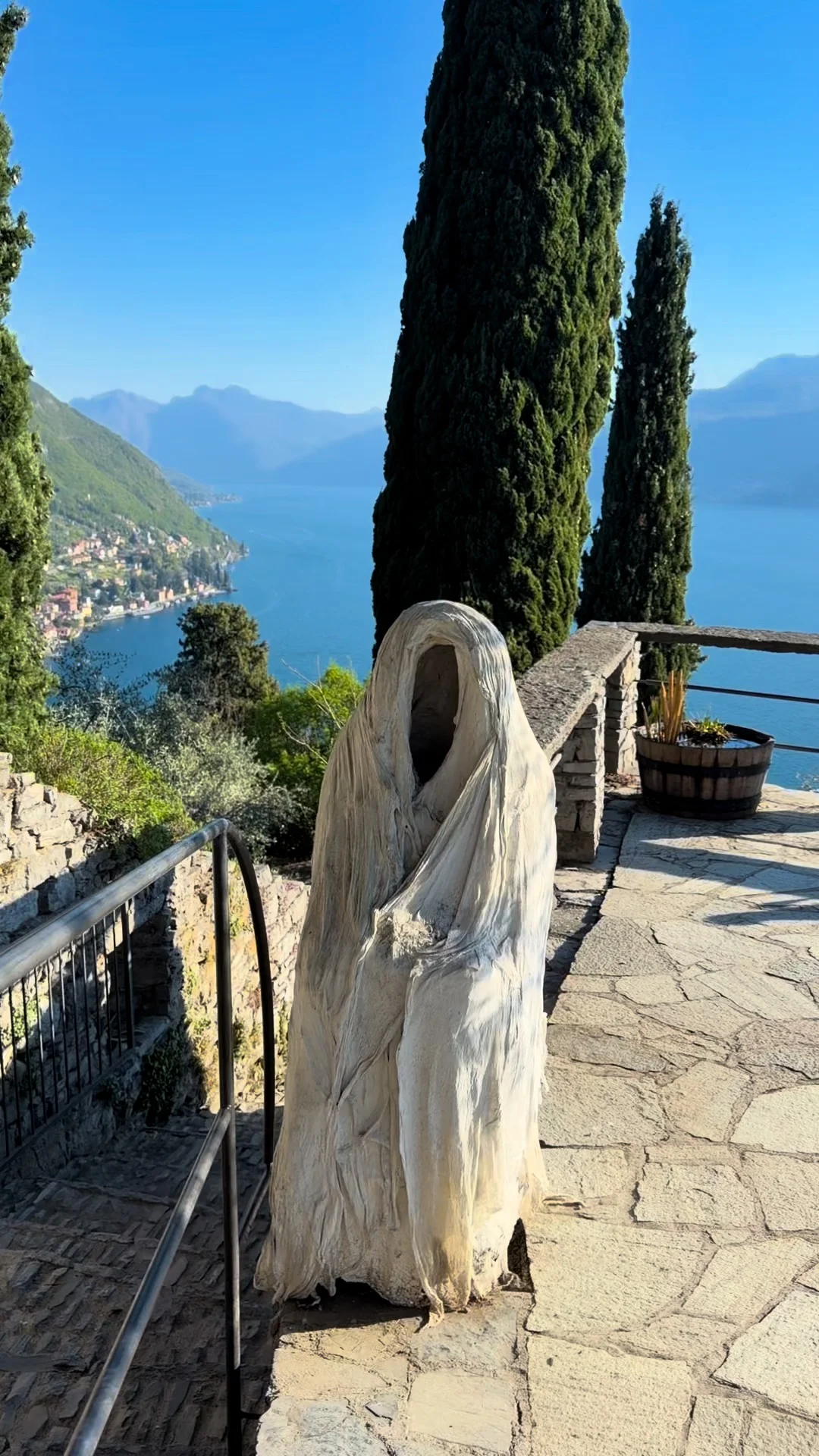 A draped sculpture beside cypress trees on a stone terrace.