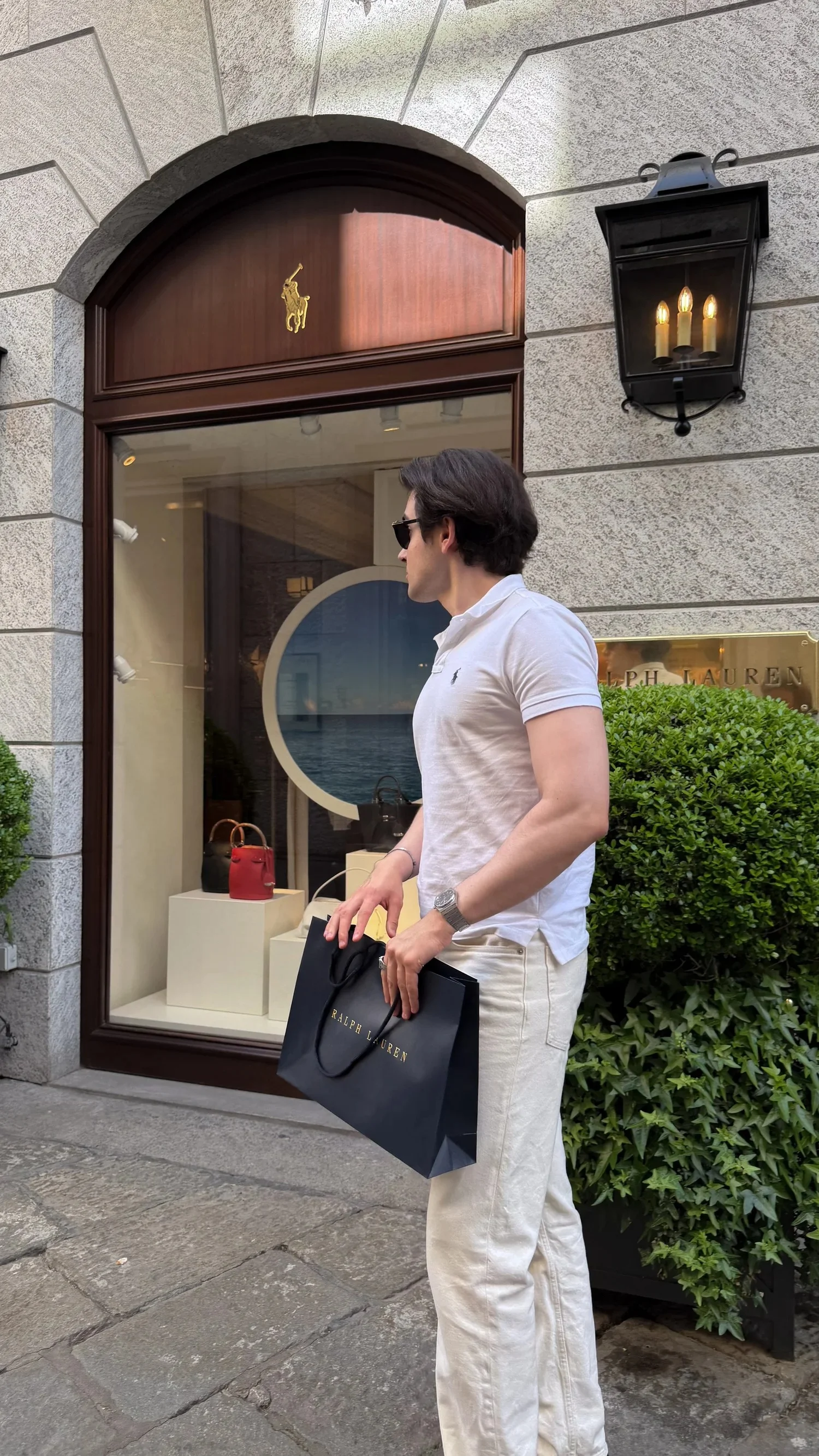 A person standing outside an arched shop entrance with a shopping bag.