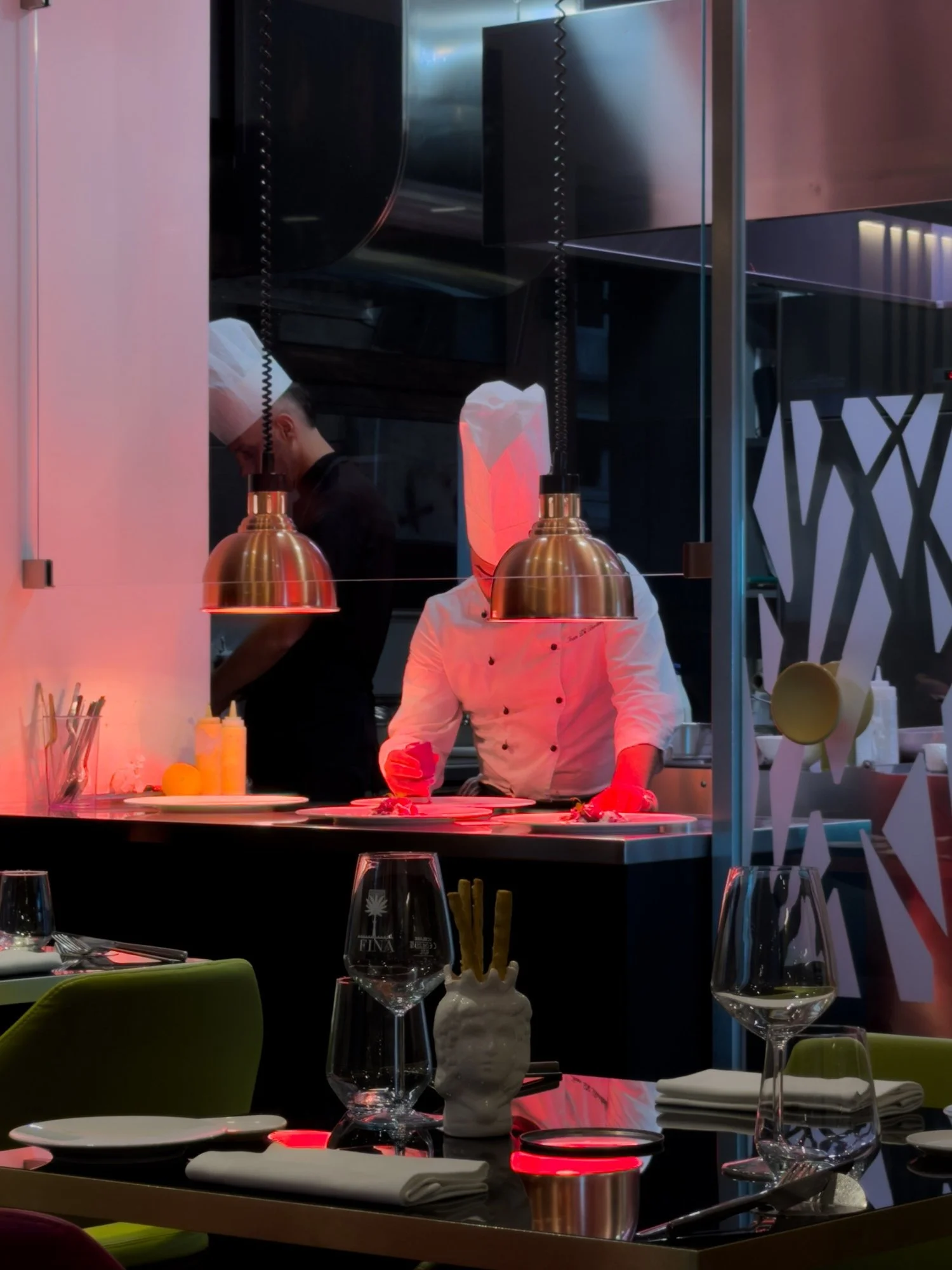 A chef working behind the illuminated kitchen counter in a dark restaurant.