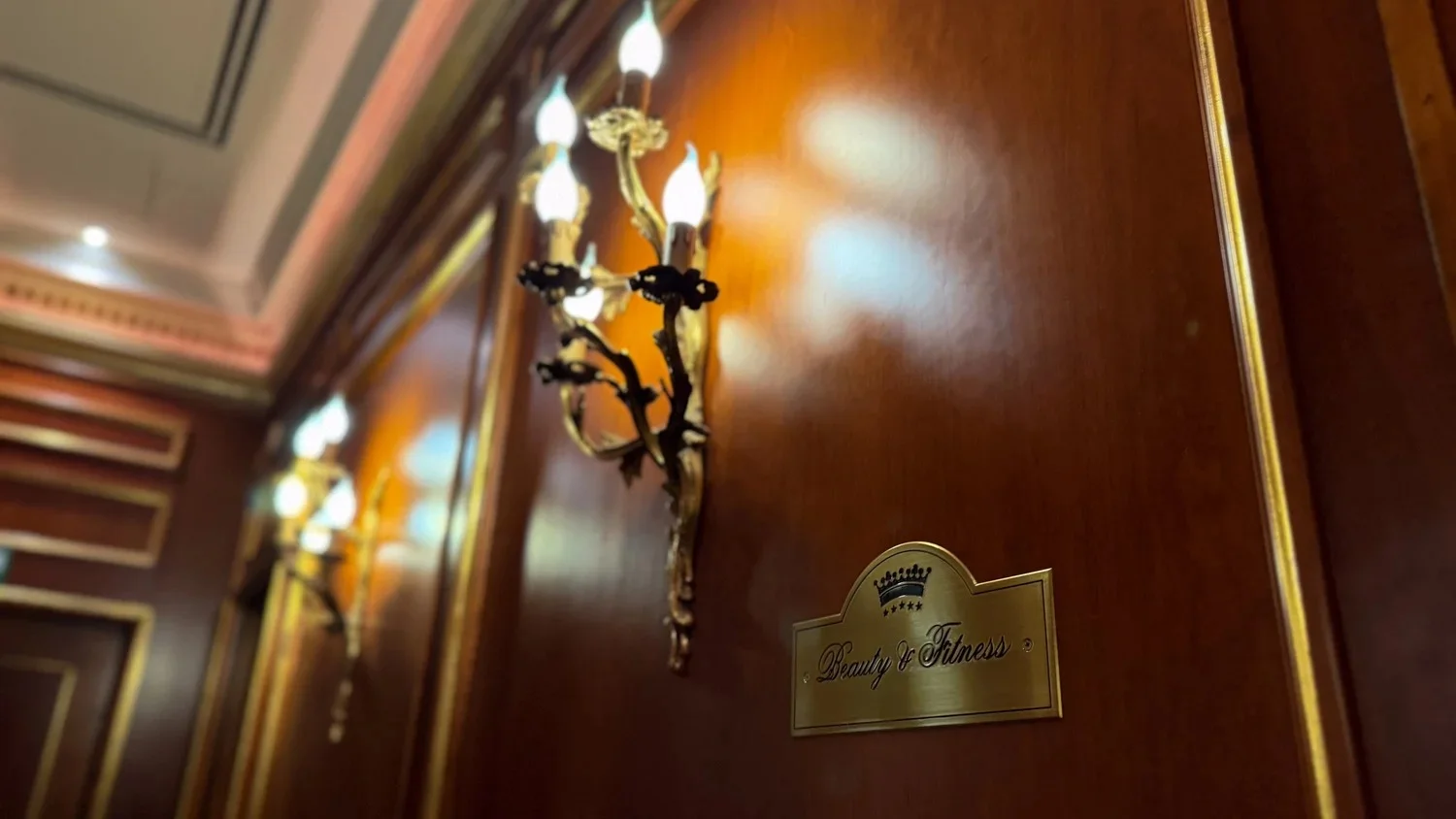 A decorative wall light and brass room plaque on polished wooden panelling.