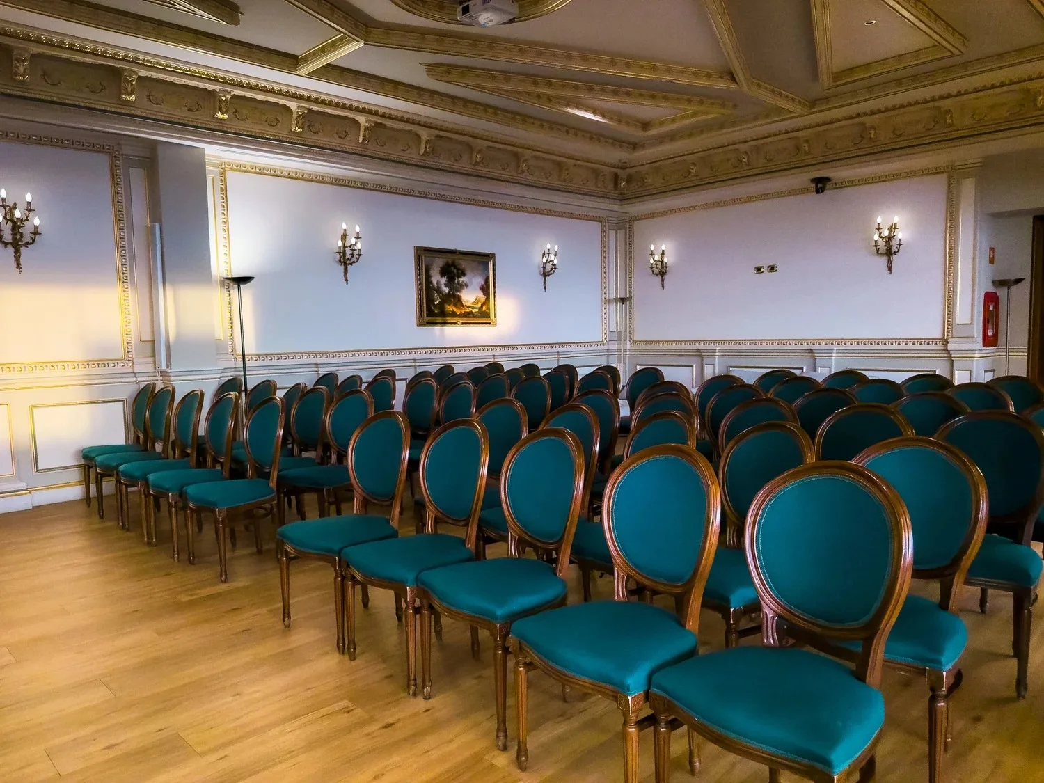 Rows of green upholstered chairs in a room with gilded mouldings.
